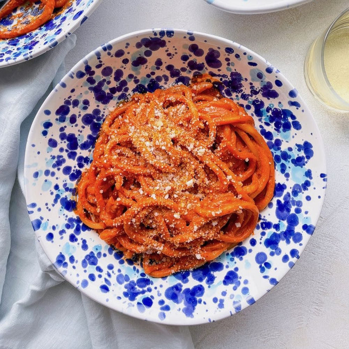 A simple pasta dish at a table setting with a hunk of cheese.