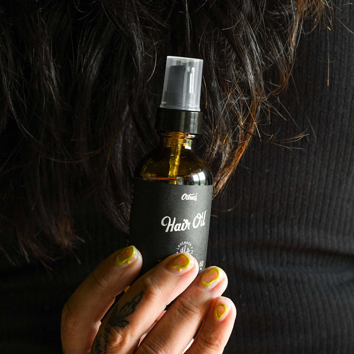 Odouds hair oil in a glass amber bottle bottle being held by a hand.