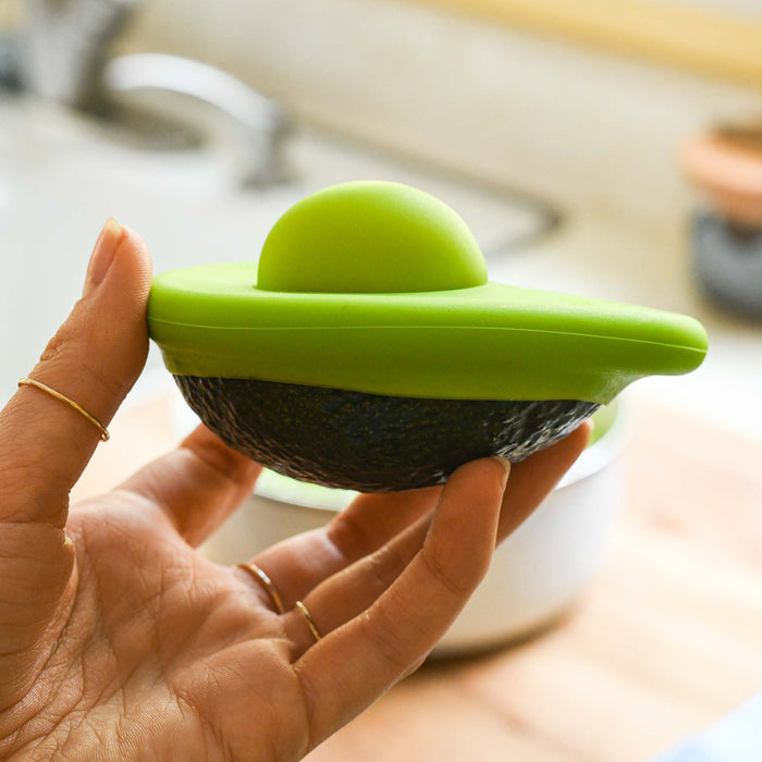 Hand holding half an avocado with the small avocado food hugger attached. From Food Huggers.