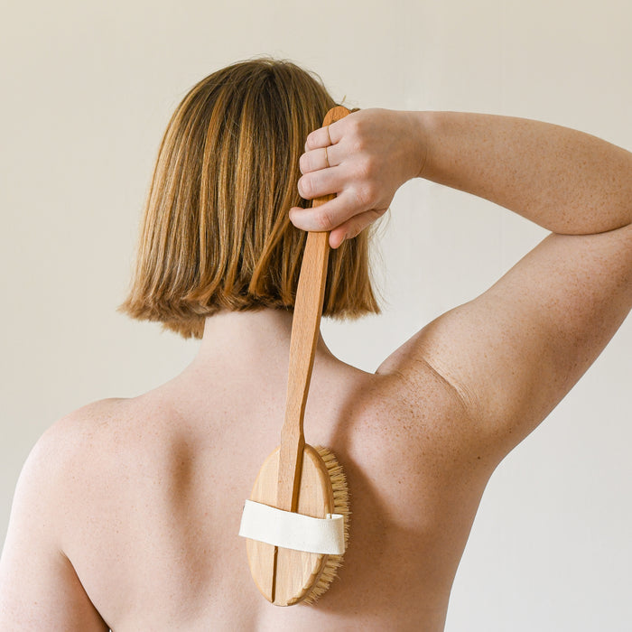 Human using a bath brush with handle to dry brush back.