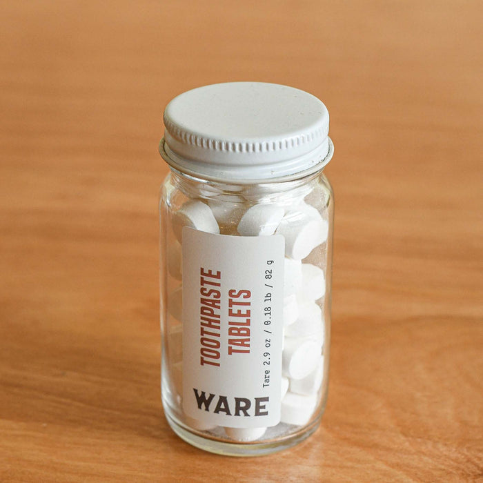 Clear glass jar with tare weights. Toothpaste tabs inside - white. Refillable.