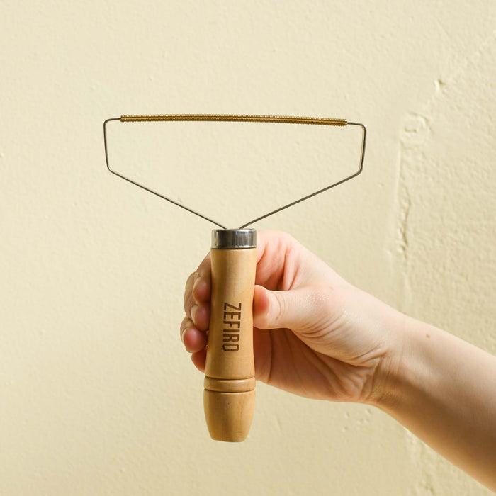 Hand holding wooden and metal hair and lint brush remover.