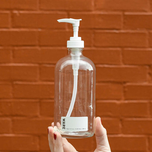Hand holding clear glass 16 oz white soap dispenser bottle. White ware label with tare weight listed. 