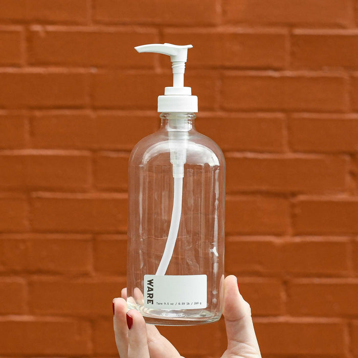 Hand holding clear glass 16 oz white soap dispenser bottle. White ware label with tare weight listed.