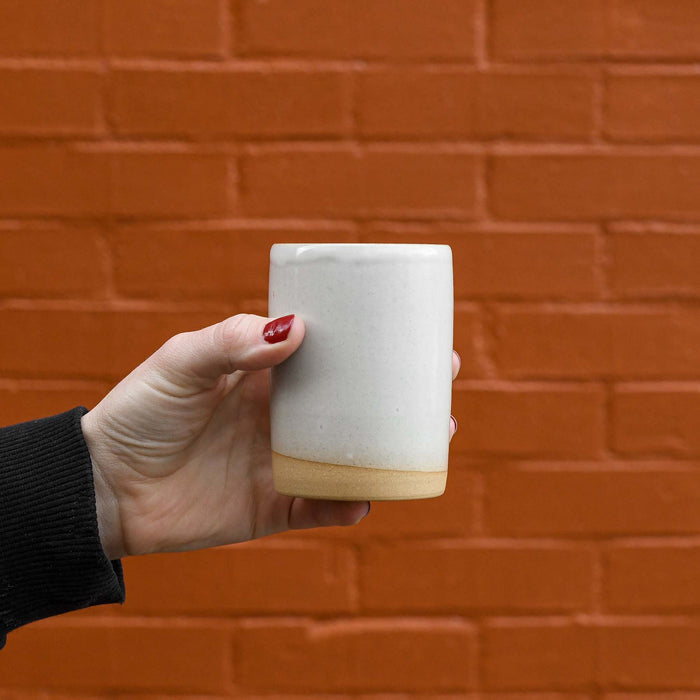 Hand holding ceramic white dipped juice cup. No handle. Made in Charleston, SC.