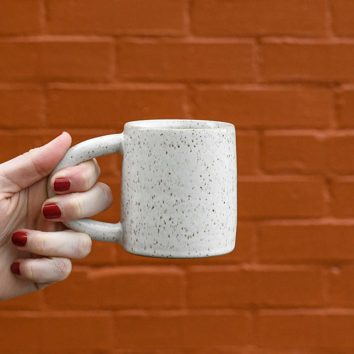Hand holding speckled white ceramic mug. Made in Charleston, SC