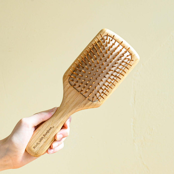 Hand holding bamboo wooden hair brush with rubber bristles.
