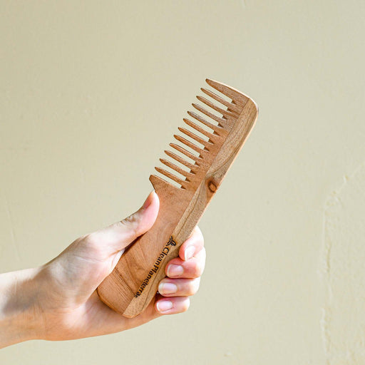 Hand holding wide tooth wooden comb.
