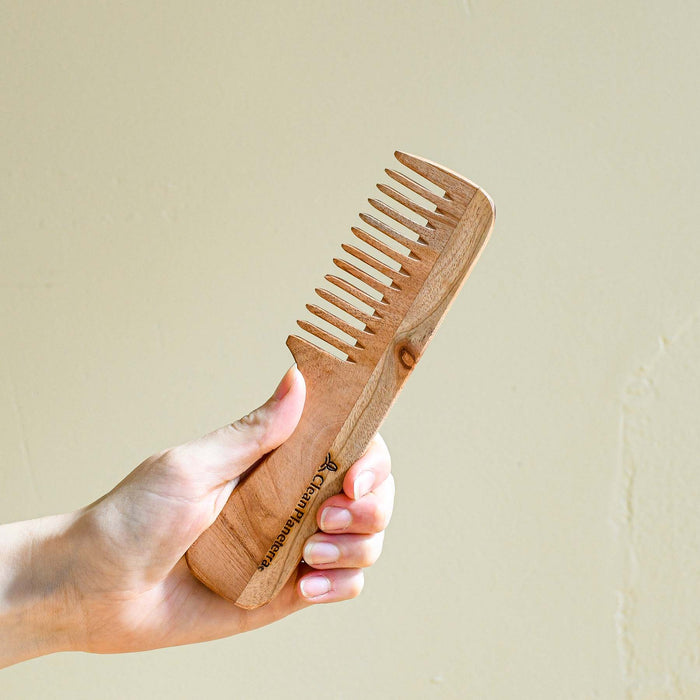Hand holding wide tooth wooden comb.
