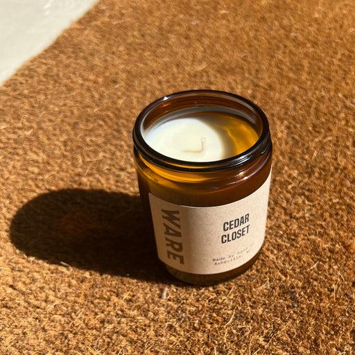 A candle in a reusable brown glass jar. It is scented with organic essential oils of lavender, cedar, bergamot, and vetiver.