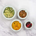 Soft white variety glass and silicone reusable food hugger lids on various bowls with food. 