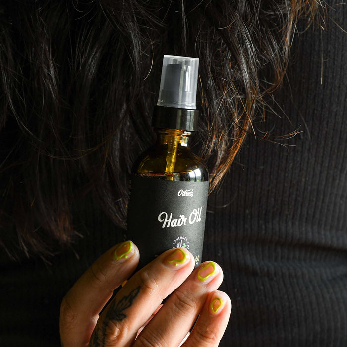 Odouds hair oil in a glass amber bottle bottle being held by a hand. 