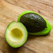 Avocado on cutting board cut in half. Pitted half face down in the small avocado food hugger. From Food Huggers.