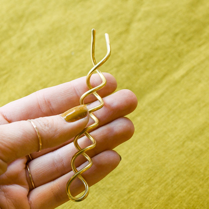 Hand holding brass bun screw for hair. 