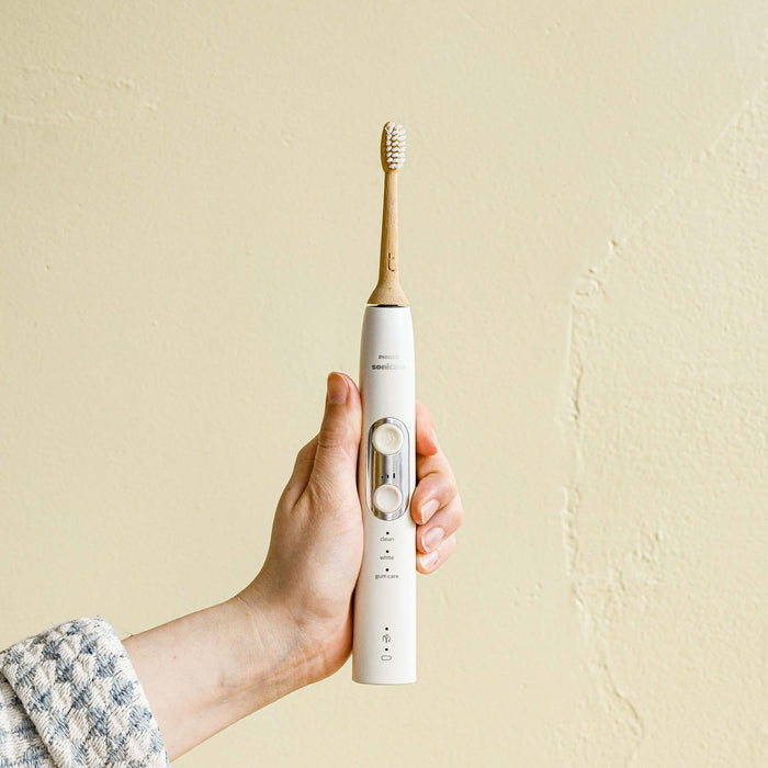 Hand holding out a Sonicare electric toothbrush with a bamboo head.