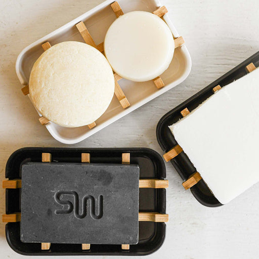 Three soap bamboo grid soap dishes. two black with one having black soap and the other with white soap. White soap dish has two white round soaps.