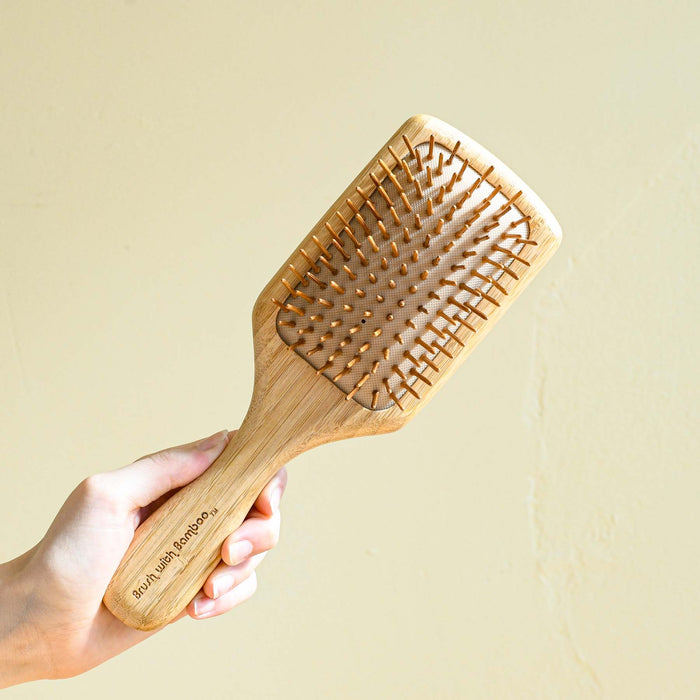 Hand holding bamboo wooden hair brush with rubber bristles. 